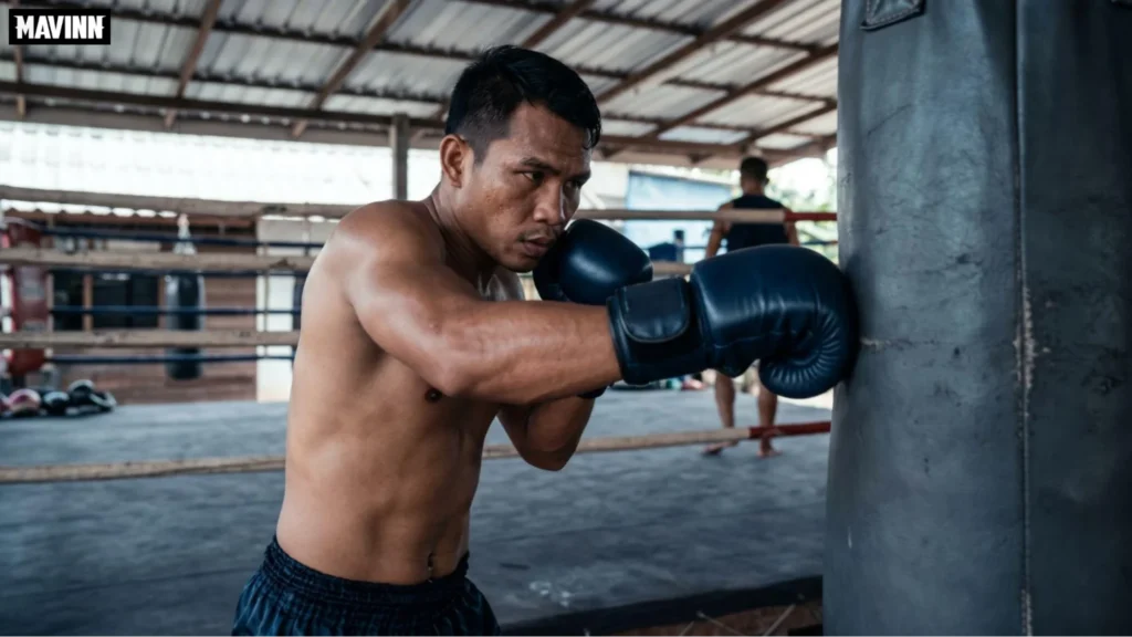 Muay Thai fighter sitting on a wooden bench in a Thailand boxing gym wrapping hands